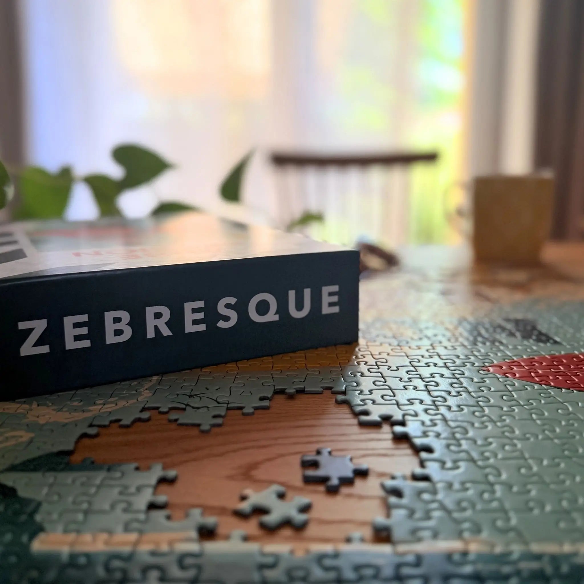Boîte de puzzle ZEBRESQUE posée sur un puzzle adulte en cours avec lumière naturelle et ambiance chaleureuse. Illustration inspirée du surf, de l’océan et des sessions matinales au bord de mer.
