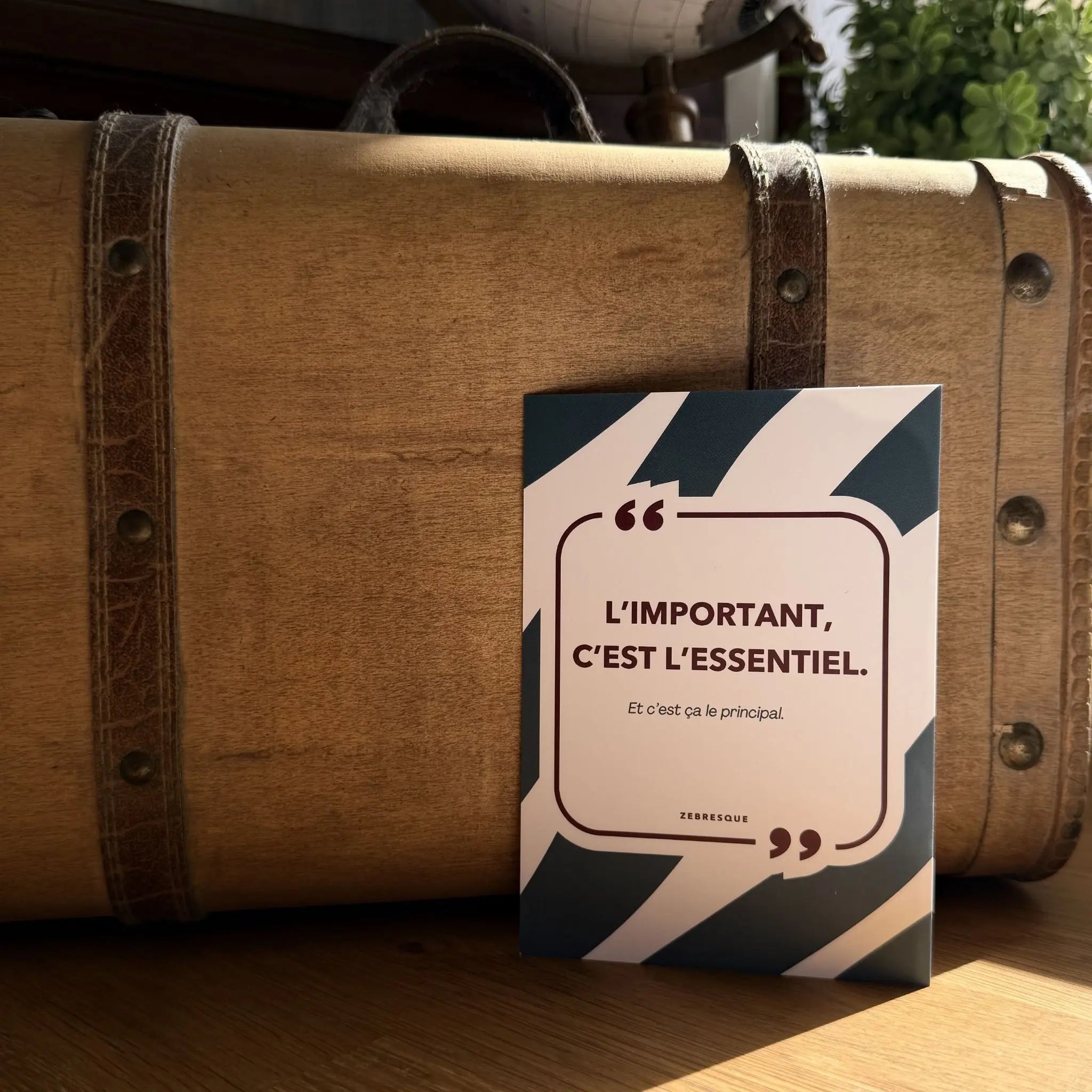 Carte postale premium ZEBRESQUE “L’important, c’est l’essentiel.” photographiée dans une ambiance vintage chaleureuse avec lumière naturelle. Une création graphique française pensée pour les amateurs de belles choses simples et de calme intérieur.
