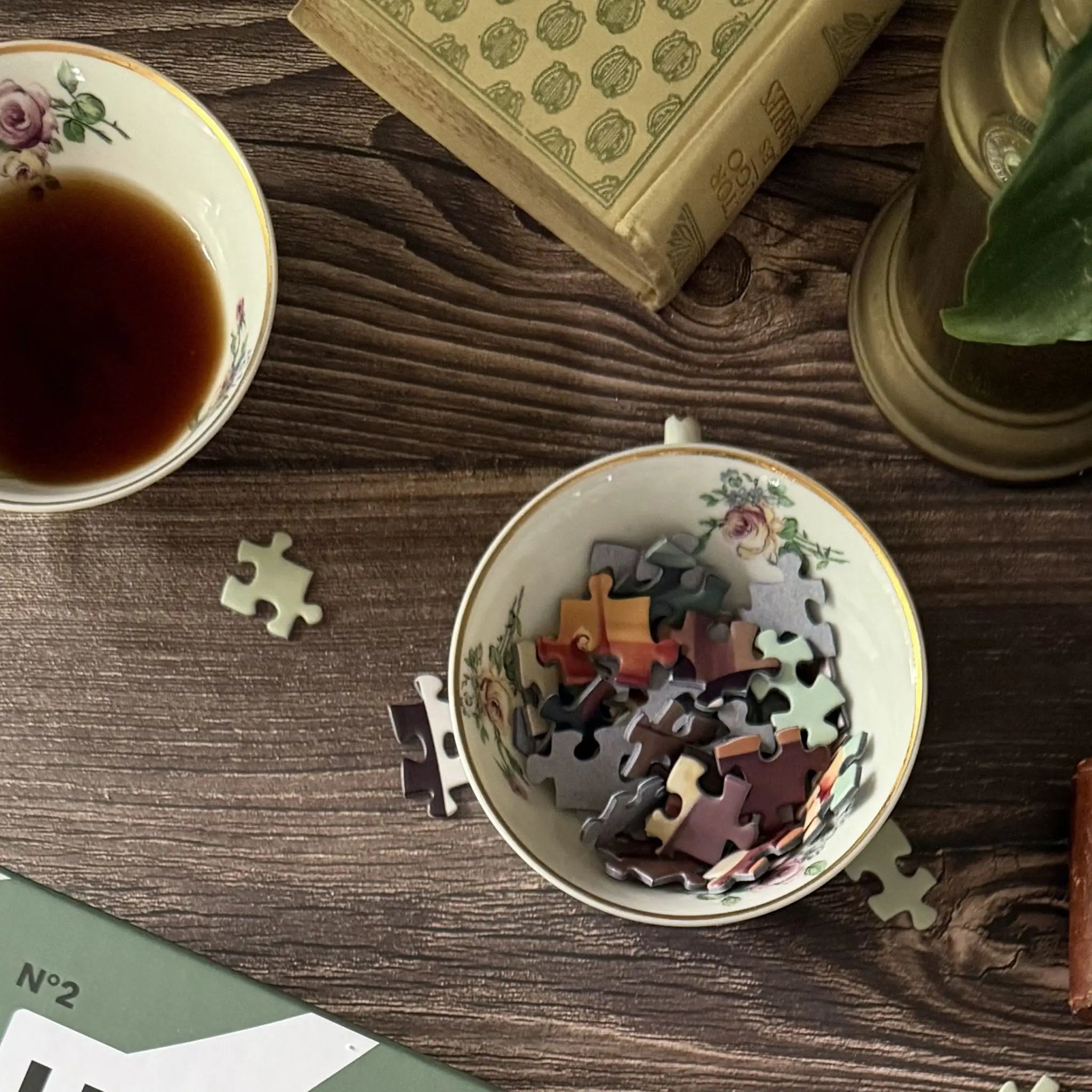 Pièces de puzzle adulte 1000 pièces ZEBRESQUE dans un bol vintage avec thé et livre ancien sur table en bois, ambiance calme et cosy pensée pour la déconnexion et le slow life en mettant en valeur un couples amoureux de personnes agées.