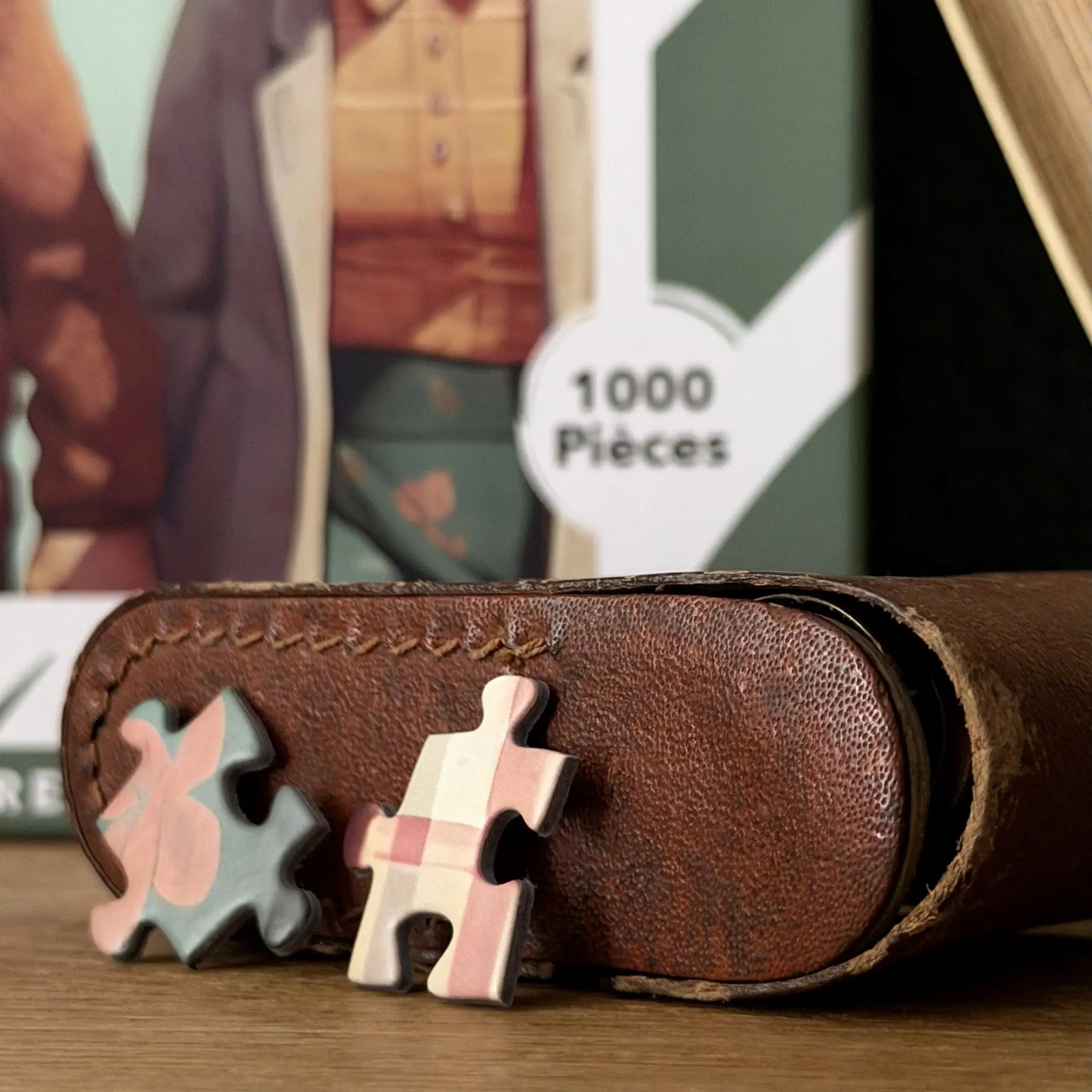 Pièces du puzzle adulte 1000 pièces ZEBRESQUE « Une belle histoire » posées sur un étui en cuir dans une ambiance rétro calme et contemplative illustrant le couple de vieux amoureux présent dans le puzzle