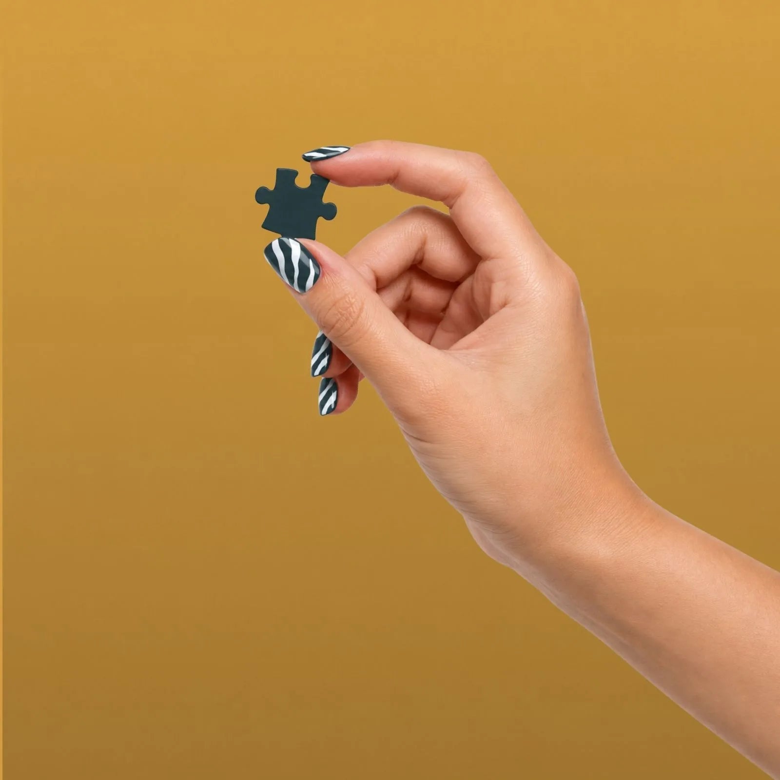 Main aux ongles rayés tenant une pièce de puzzle vert foncé, dans l’univers de ZEBRESQUE, marque française de puzzles et d’objets singuliers pour les esprits atypiques, HPI, TDAH et hypersensibles.