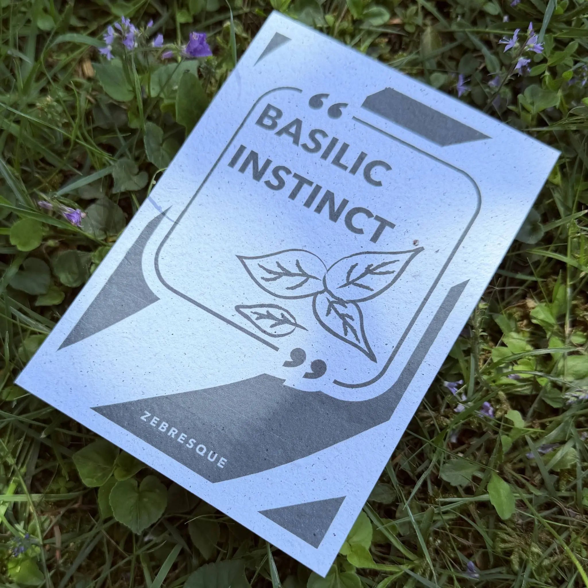 Carte à planter “Basilic instinct” posée dans l’herbe parmi des fleurs sauvages. Papeterie à planter ZEBRESQUE en papier recyclé avec graines de basilic, pensée pour les esprits sensibles, créatifs et contemplatifs.