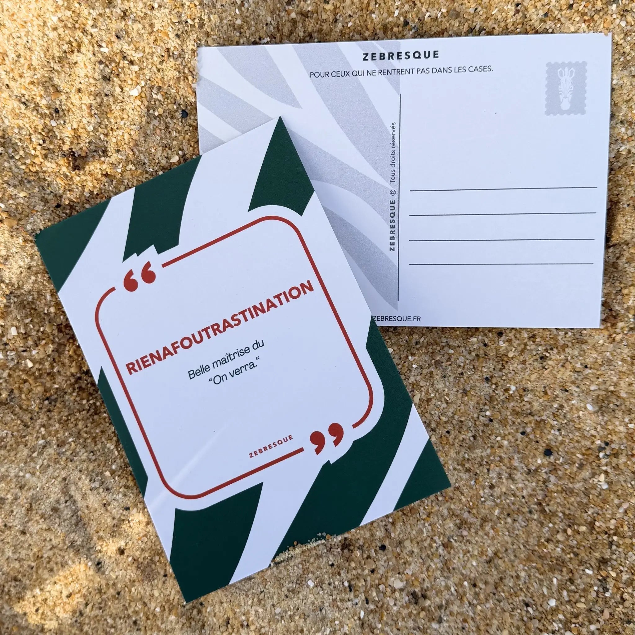 Carte postale premium ZEBRESQUE “Rienafoutrastination” photographiée sur le sable avec lumière naturelle. Papeterie décalée et poétique pour ceux qui pensent beaucoup, remettent parfois à demain et transforment les petits chaos mentaux en art de vivre.