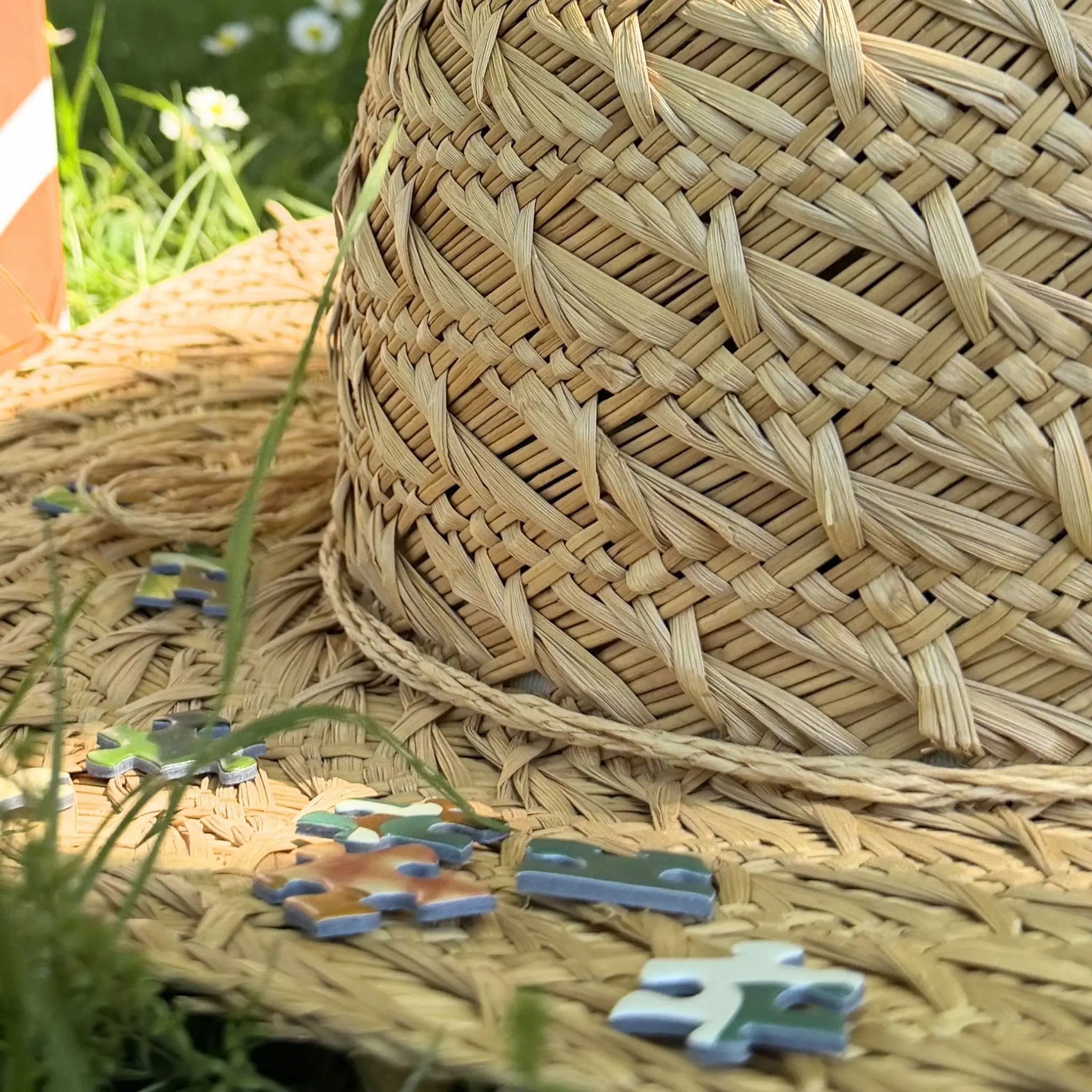 Détail de pièces du puzzle adulte ZEBRESQUE posées sur un chapeau de paille tressé dans l’herbe, ambiance estivale naturelle et apaisante autour du puzzle “M’aimer dans les orties”.