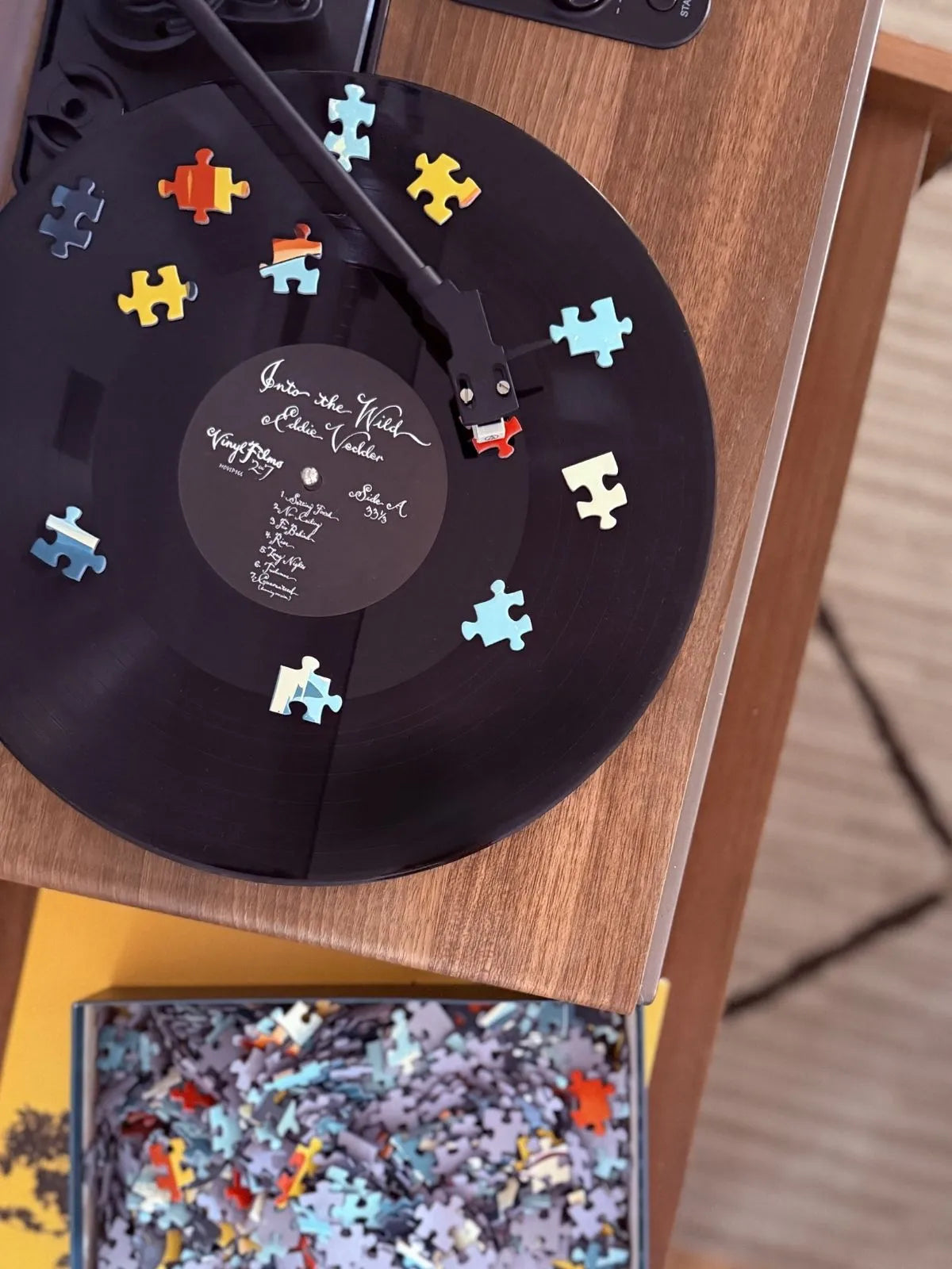 Tourne-disque vintage entouré de pièces de puzzle colorées ZEBRESQUE. Une ambiance musicale calme et nostalgique pensée pour accompagner les puzzles adultes 1000 pièces et les longues pauses sans notifications.