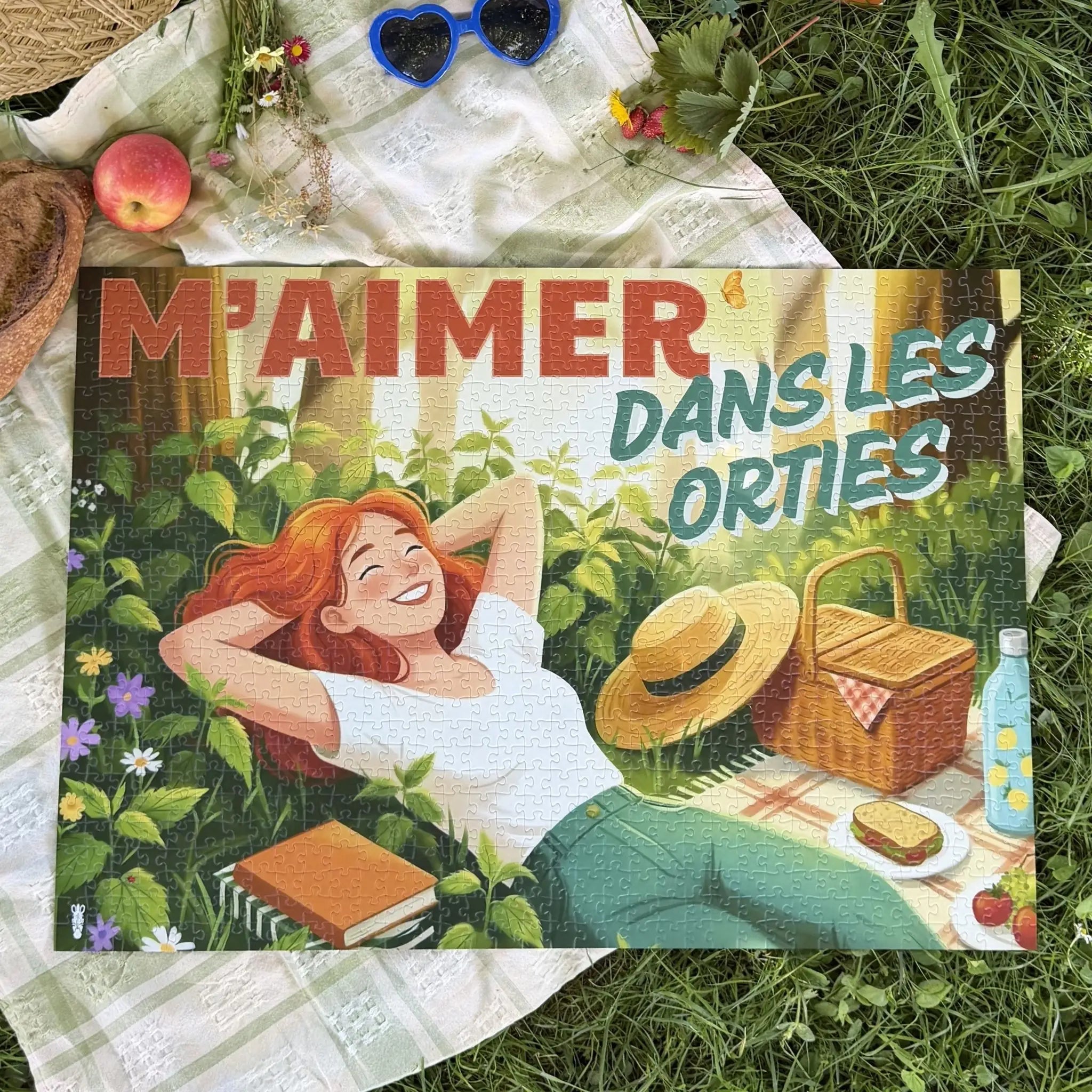 Puzzle adulte 1000 pièces ZEBRESQUE “M’aimer dans les orties” terminé sur une couverture de pique-nique dans l’herbe avec panier en osier, fleurs, lunettes en forme de cœur et ambiance estivale nature. Illustration féminine autour du calme, de la déconnexion et du slow life