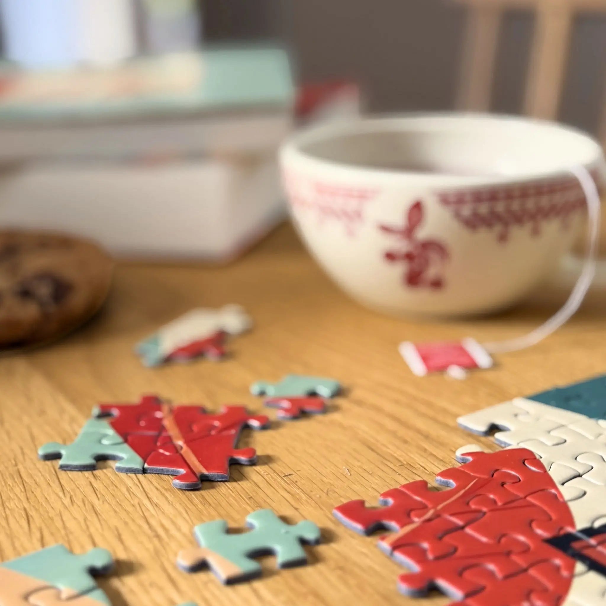 Détail d’un puzzle feminin adulte 1000 pièces ZEBRESQUE representant 3 femmes au repos sur une table en bois avec tasse de thé, livre et pièces de puzzle dans une ambiance cosy, cocooning et slow life.