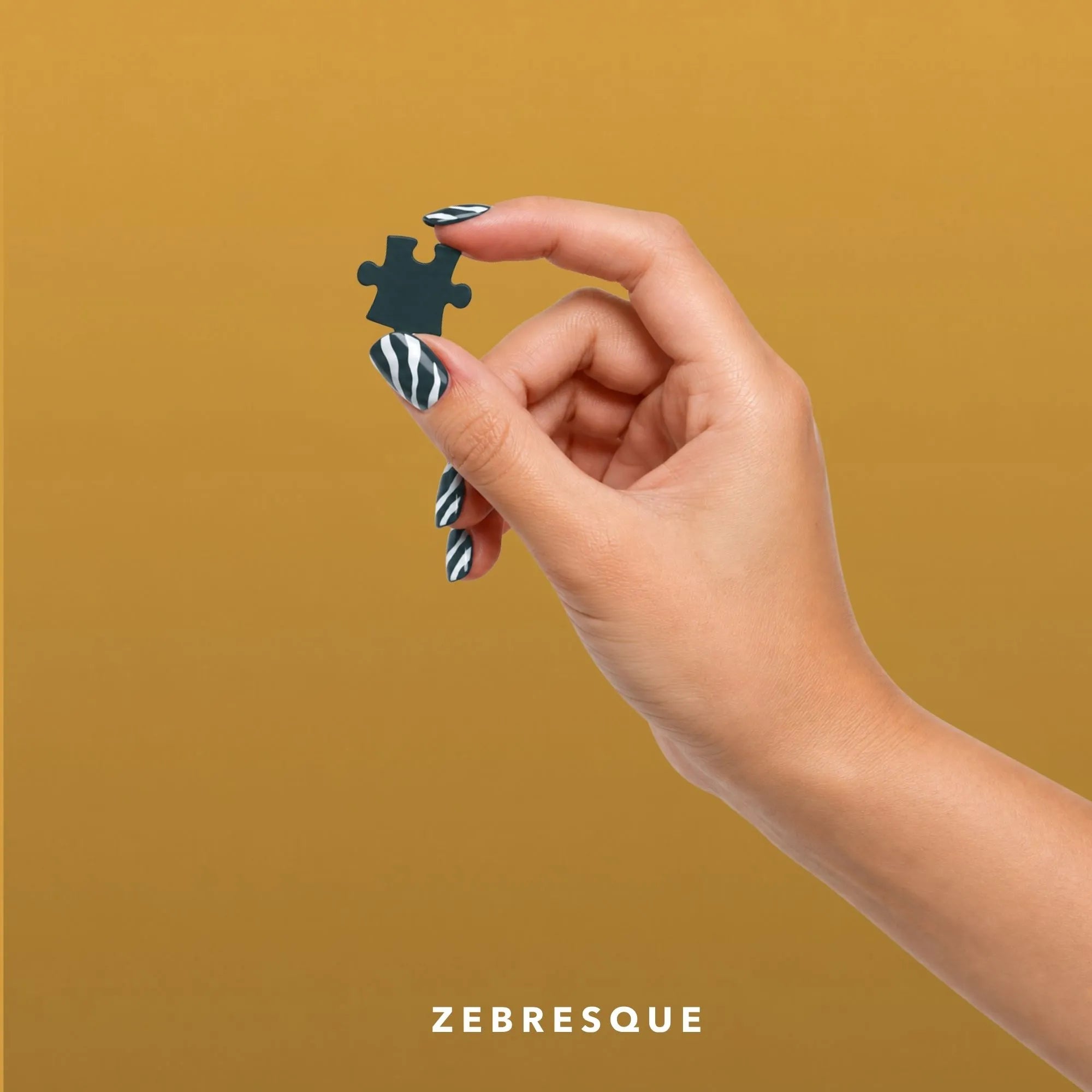 Main aux ongles rayés tenant une pièce de puzzle vert foncé, dans l’univers de ZEBRESQUE, marque française de puzzles et d’objets singuliers pour les esprits atypiques, HPI, TDAH et hypersensibles.